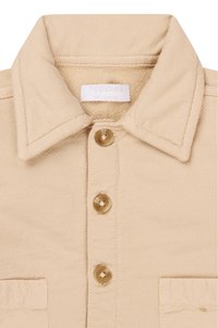 Beige Hemd mit strukturiertem Kragen, vier Knöpfen und einer Brusttasche. Hergestellt aus strukturierter матери ял с sichtbaren Nähdetails.