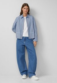 Zila un baltā svītraina jakas ar bezpogām priekšpusi un divām priekšējām kabatām, apvienota ar brīvāka piegriezuma zilām džinsām un baltām apaviem.