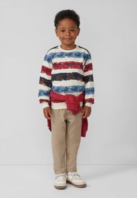 Sudadera a rayas multicolores en azul, rojo y blanco con un patrón floral, combinada con pantalones beiges y zapatos blancos. Suéter rojo anudado.