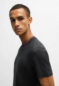 Black short-sleeve T-shirt with a crew neck, featuring a textured pink ribbed collar. Smooth fabric, fitted design. No visible logos or patterns.