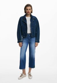 Jeansjacka i mörkblått med en kortad passform, ihopparad med ljusblå jeans med blommönster broderat på benen och vita snörskor.