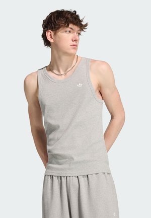 Jonge man met kort krullend haar, die een lichtgrijze mouwloze geribbelde tanktop en bijpassende korte broek draagt, kijkt opzij.