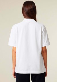 Witte polo met korte mouwen, rechte snit, ribbelkraag en zijsplitten. Zachte katoenen stof. De achterzijde toont een minimalistisch ontwerp.