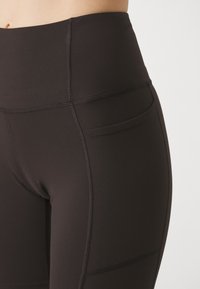 Schwarze, hochtaillierte Leggings aus dehnbarem Stoff, mit einer glatten Textur, flachen Nähten und einer Seitentasche.