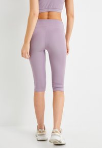 Lila caprileggings med en slät textur, figursydd design och midjehöjd, kombinerade med vita träningsskor.
