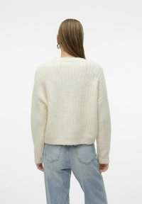 Kreemikas värvi kudum sweater tekstureeritud ribakujundusega, lühendatud hemiga ja langevate õlgadega, koos helesiniste denimpükstega.