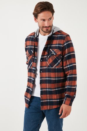 Flanellen shirt in een oranje, marineblauw en witte ruitpatroon. Bevat een grijze capuchon, twee voorzakken en een knoopsluiting. Zachte textuur.