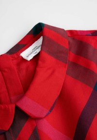 Kołnierzyk i dekolt czerwonej kraciastej koszuli z ciemnymi i jasnymi paskami, z widoczną białą metką wewnątrz kołnierza.