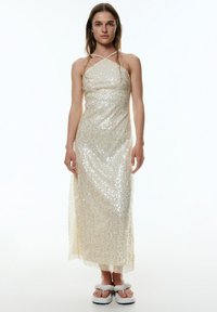 Paillettenverziertes cremefarbenes Kleid mit tailliertem Oberteil und fließendem, knöchellangem Rock; verfügt über dünne überkreuzte Träger und einen transparenten Überwurf.