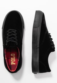 Mustat samettitossut, joissa on teksturoitu musta kumipohja, mustat nauhat ja punamustaruudullinen vuori, jossa lukee "POLO". Litteä muotoilu, matala tyyli.