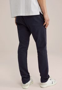 Pantaloni din bumbac de culoare albastru marin, cu croi drept, purtați cu adidași albi. Țesătura pare netedă, cu detalii minime.