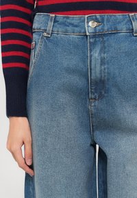 Jeans di denim azzurro chiaro a vita alta, con una linea dritta, dotati di chiusura con bottone argentato e dettagli di cucitura sottile.