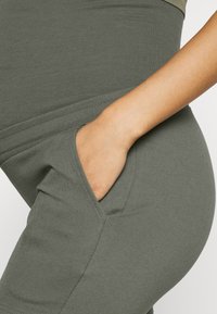 Kalhoty z bavlněné směsi olivové zelené barvy se boční kapsou, s hladkou texturou a elastickým střihem pro pohodlí a funkčnost.