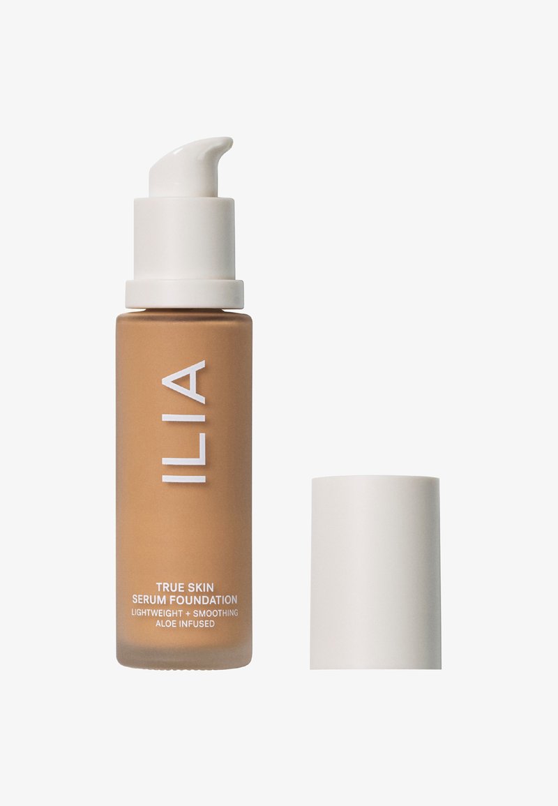 Botella de ILIA True Skin Serum Foundation en un tono marrón suave, con un dosificador y tapa blancos. El diseño es elegante con texto minimalista.