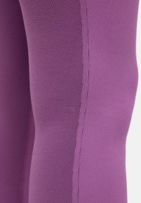 Nahaufnahme eines lila strukturierten Stoffes mit kontrastierenden Strickmustern und einer vertikal verlaufenden genähten Naht.