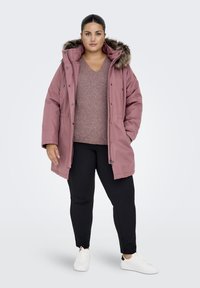 Pink padded parka with fur-trimmed hood, front snap buttons, layered over a light sweater, paired with black pants and white sneakers.