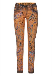 Jean slim orange avec éclaboussures de peinture noires, bleues et roses, texte style graffiti et détails cloutés sur les poches avant, ceinture marquée.