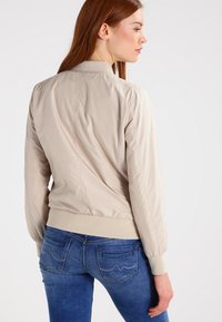 Beige bomberjack met geribbelde zoom en manchetten, met een gladde, glimmende textuur en stijlvolle stiksels aan de achterkant.