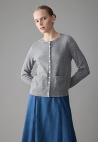 Grå ullcardigan med knäppning, rund halsringning, två fickor och långa ärmar. Matchas med en blå denimkjol.