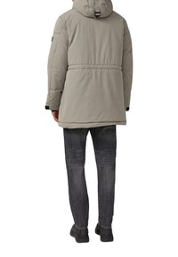 Gepolsterte hellgraue Jacke mit Kapuze, tailliertem Schnitt, elastischen Bündchen und glatter, matter Oberfläche. Kombiniert mit dunklen Jeans und Stiefeln.