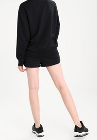 Conjunto de sudadera negra y pantalones cortos, con un ajuste relajado. Tela suave, mangas cortas y escote redondo. Usado con zapatillas deportivas negras.