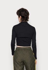 Haut noir à manches longues coupé, avec un col montant, associé à un pantalon vert matelassé avec une bande latérale jaune. Texture du tissu lisse.