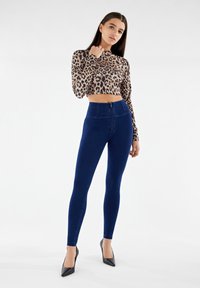 Crop top a maniche lunghe con stampa leopardata e collo alto, abbinato a jeans skinny a vita alta blu scuro e décolleté neri a punta.