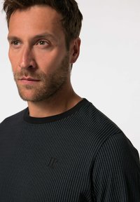 Jersey a rayas negras con un patrón texturizado, cuello redondo y un sutil detalle de logo en el pecho, hecho de una tela suave y transpirable.
