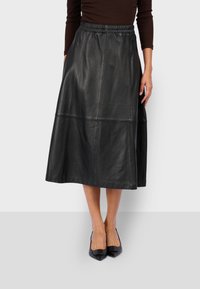Gonna midi in pelle nera con vita elastica, caratterizzata da una texture liscia e un design a pannelli. Indossata con scarpe nere a punta.