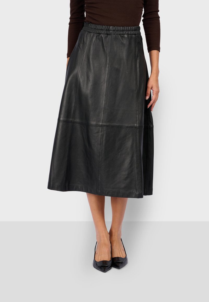 Gonna midi in pelle nera con vita elastica, caratterizzata da una texture liscia e un design a pannelli. Indossata con scarpe nere a punta.