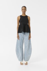 Top nero senza maniche con design peplum abbinato a jeans oversize azzurri, con una texture in denim sbiadito e orli frangiati.