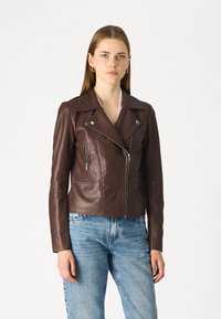 Brun skinnsykkeljakke med glidelåslommer, slagkrage og tettsittende design, båret over lyseblå jeans. Glatt tekstur og skreddersydd passform.
