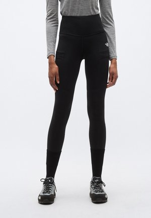 Kõrge vöökohaga mustad retuusid sujuva tekstuuriga, kahe küljetaskuga ja keha järgiva lõikega, kombineeritud halli pika varrukaga särgi ja matkasaabastega.