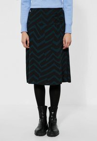 Černá sukně s tyrkysovým cik-cak vzorem, se skládacím detailem na boku. Nosí se s černými punčochami a kotníkovými botami.