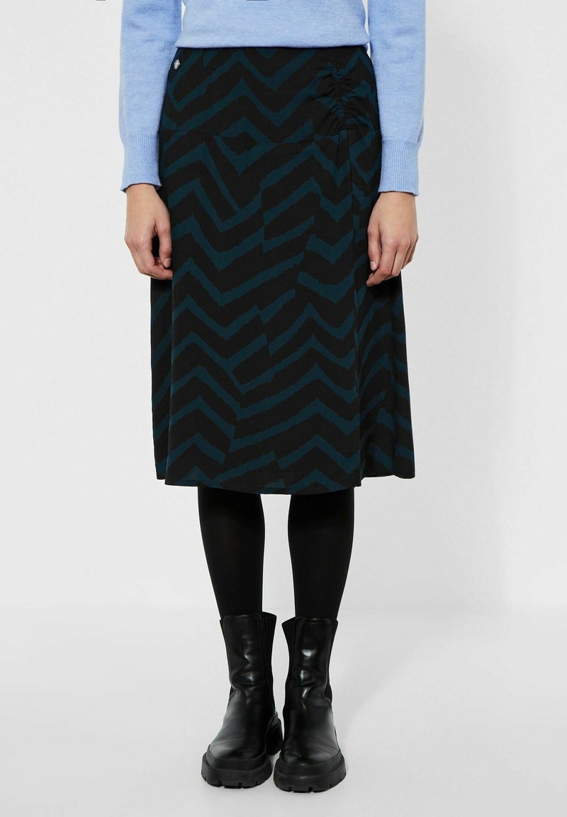 Černá sukně s tyrkysovým cik-cak vzorem, se skládacím detailem na boku. Nosí se s černými punčochami a kotníkovými botami.