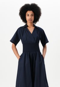 Vestido azul marinho com mangas curtas, decote em V e cintura franzida. Apresenta bolsos e uma saia fluida. Tecido suave com um brilho subtil.
