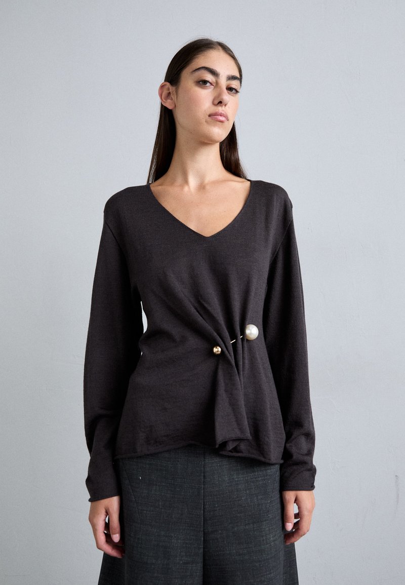 Dark gray long-sleeve top with a V-neck, featuring a twisted front detail and gold and pearl accents near the waistline. Smooth texture.
