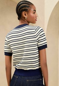 Maglione a righe navy e crema a maniche corte con scollatura e orlo a coste, tessuto testurizzato, design aderente, indossato con denim scuro.