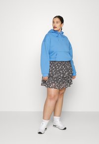 Hoodie azul claro com um bolso frontal e cordão, combinado com uma saia preta em camadas com um padrão floral branco, usada com ténis brancos.