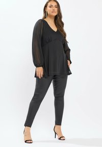 Haut noir avec un col en V et des manches longues transparentes, associé à un pantalon noir moulant et des talons aiguilles noirs. Tissu doux, coupe relaxée.