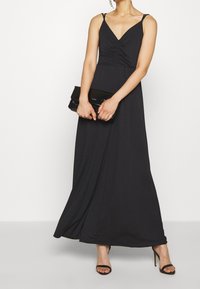 Mustapuku, jossa on ohuet olkaimet, nyrkkiyksikkö ja virtaava hame. Yhdistetty tyylikkään mustan clutch-laukun ja nauhaliukujen kanssa.