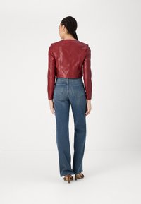 Giacca cropped in pelle rossa con maniche lunghe, abbinata a jeans blue a vita alta. Vestibilità su misura e dettagli di cucitura discreti.
