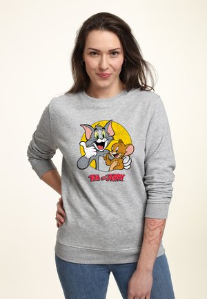 Felpa grigia con una grafica di Tom e Jerry su uno sfondo giallo. Maniche lunghe con polsini a costine, vestibilità comoda e colletto rotondo.