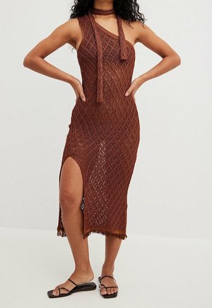 Ærmeløs brun strikket midikjole med sideslids og matchende nakkebånd, båret med sorte flade sandaler med stropper.