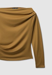 Top con spalle scoperte e maniche lunghe in un caldo colore senape. Realizzato in tessuto leggero e morbido con dettagli drappeggiati sul davanti.