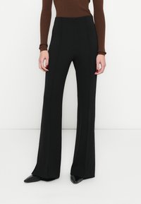 Čierne široké nohavice z hladkého materiálu, s vysokým pásom a prednými záhybmi, v kombinácii s čiernymi lodičkami so špicatou špičkou.