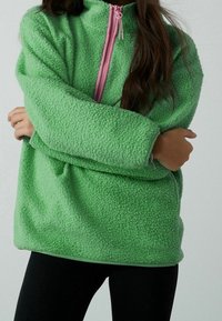 Pullover verde in pile con colletto alto e chiusura a mezza zip, caratterizzato da una texture morbida e dettagli in rosa sulla zip.