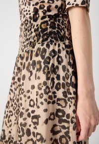 Robe imprimée léopard en tissu semi-transparent, avec une taille smockée noire, une texture plissée et des nuances variables de marron et de beige.