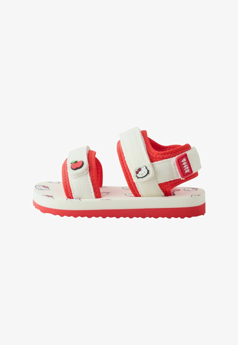 Sandale rouge et blanche pour enfant à bout ouvert avec des brides réglables, ornée de décorations Hello Kitty et pomme sur une semelle à motifs.