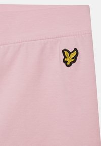 Tecido de algodão rosa claro com uma faixa elástica na cintura, apresentando um logótipo de águia bordado em preto e dourado no lado direito.